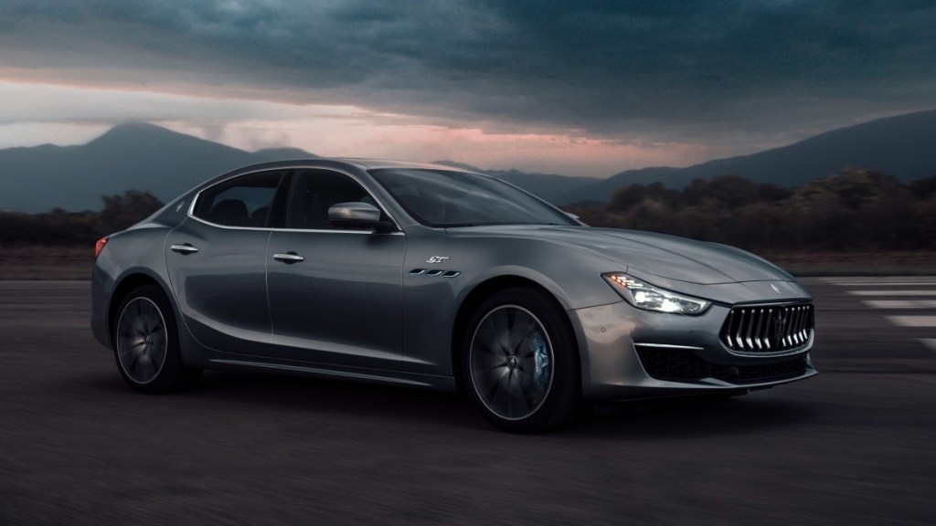 a silver 2022 maserati ghibli gt drives along a road at sunset