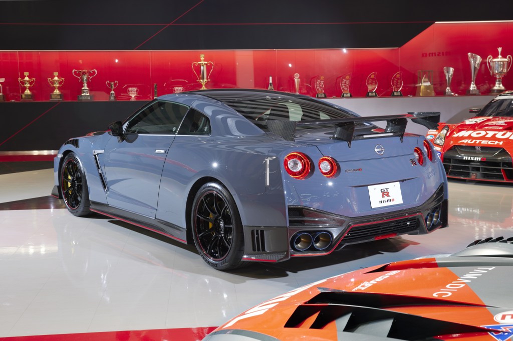 The rear 3/4 view of a blue 2022 Nissan GT-R NISMO Special Edition in a garage by some trophies