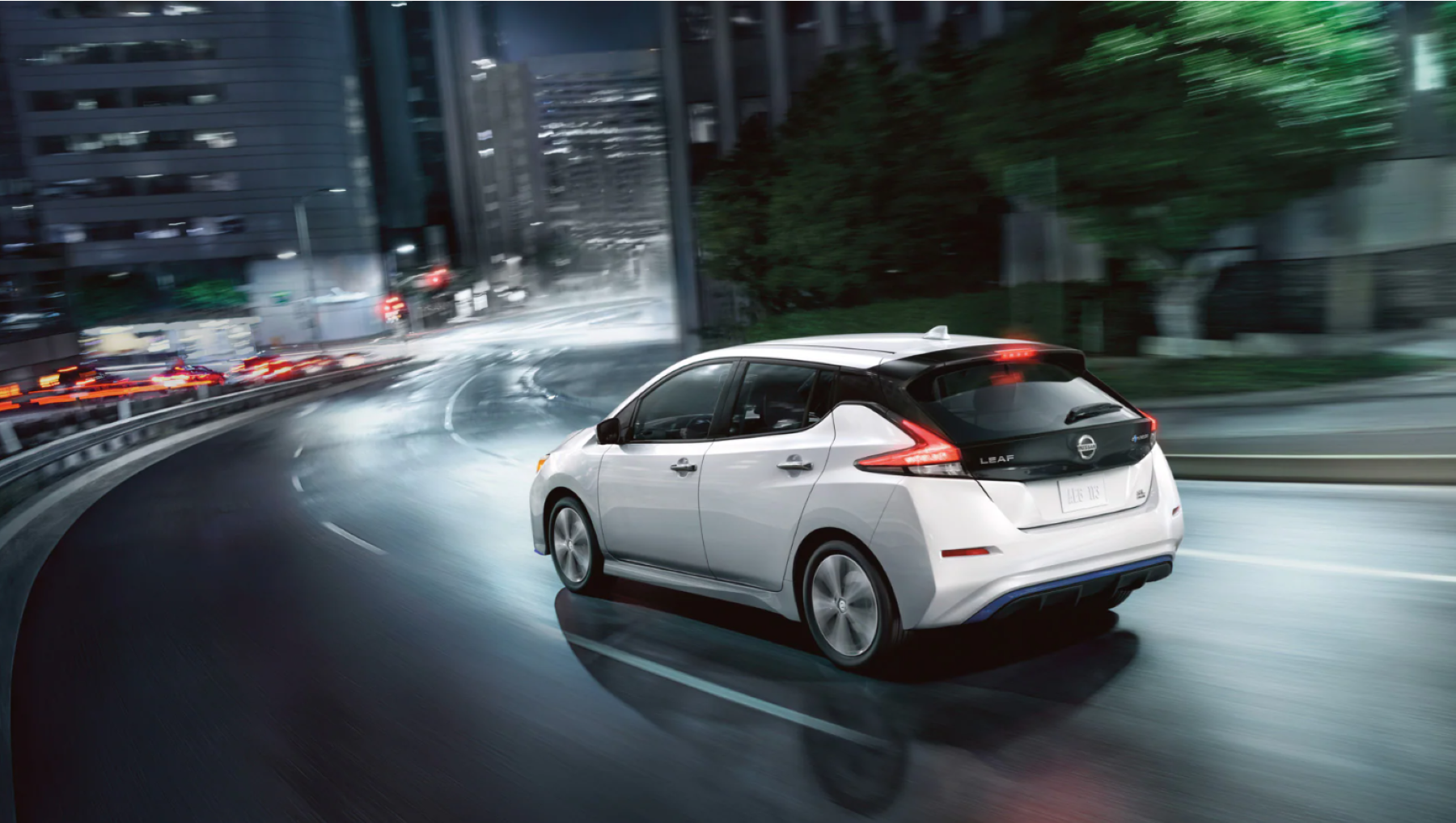A white 2022 Nissan Leaf electric vehicle (EV) driving through a city at night