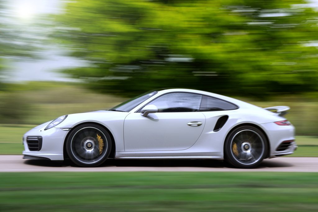 Side view of a white 2022 Porsche 911 Turbo S speeding on a country road