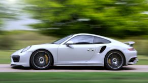 The side view of a white 2022 Porsche 911 Turbo S speeding down a country road