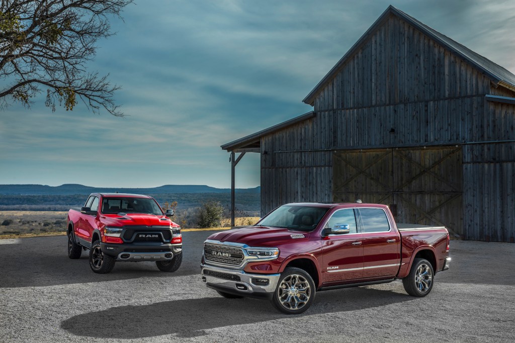 Two red Ram 1500 pickup trucks parked in front of a barn.