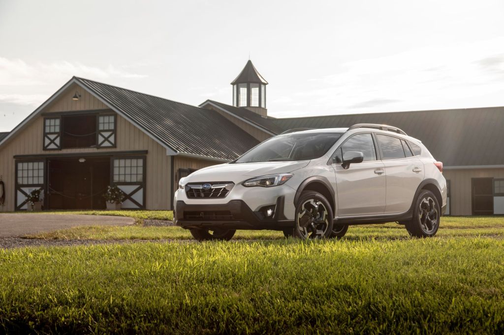A white 2022 Subaru Crosstrek in a green field with a barn behind it and is a part of the car sales industry.
