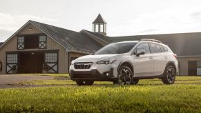 A white 2022 Subaru Crosstrek in a green field with a barn behind it that is a part of the car sales industry.