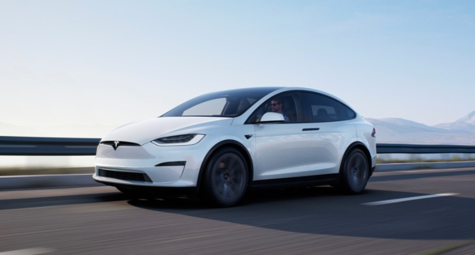 A white 2022 Tesla Model X electric luxury midsize SUV is driving on the road. 