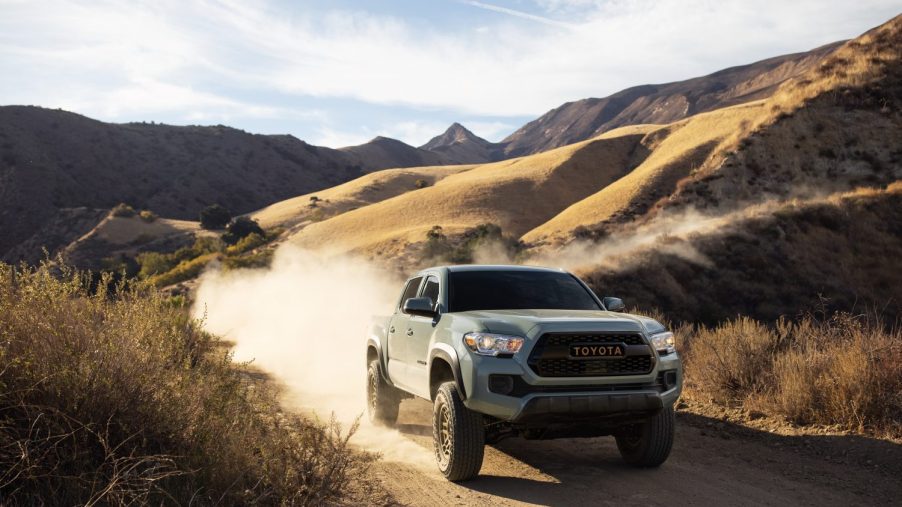 A midsize Toyota Tacoma pickup truck drives along a dirt, mountain road.