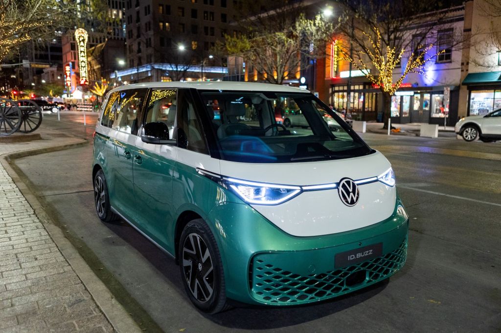 A white and green 2022 Volkswagen ID. Buzz parked on a well let street at night. 