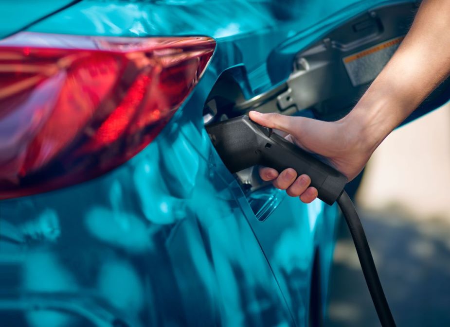 A person plugs a charging cable into the charging port of a teal 2022 Toyota Prius Prime