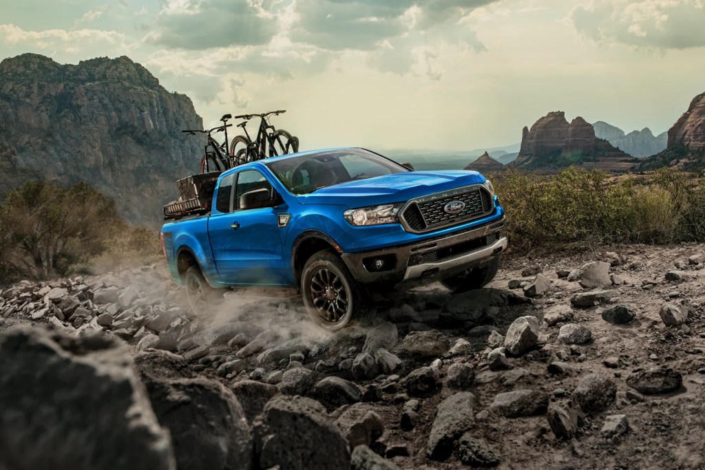 A blue Ford Ranger mid-size truck hauls two bikes and some other gear in its bed.