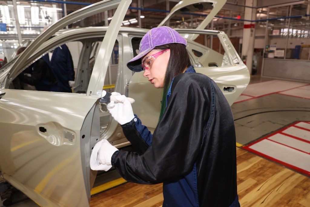 A technician touching-up the paint on a 2023 Acura Integra on a factory floor.