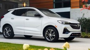 A white 2023 Buick Encore GX subcompact crossover SUV model parked on a driveway near flowerbeds