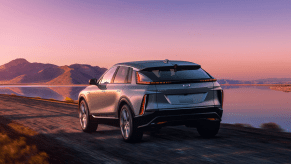 A rearview shot of a gray 2023 Cadillac Lyriq luxury electric SUV model driving near a lake at sunset