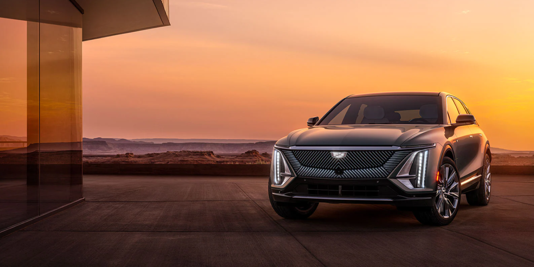 A gray 2023 Cadillac Lyriq luxury electric SUV model parked outside of a luxury house during a sunset sky