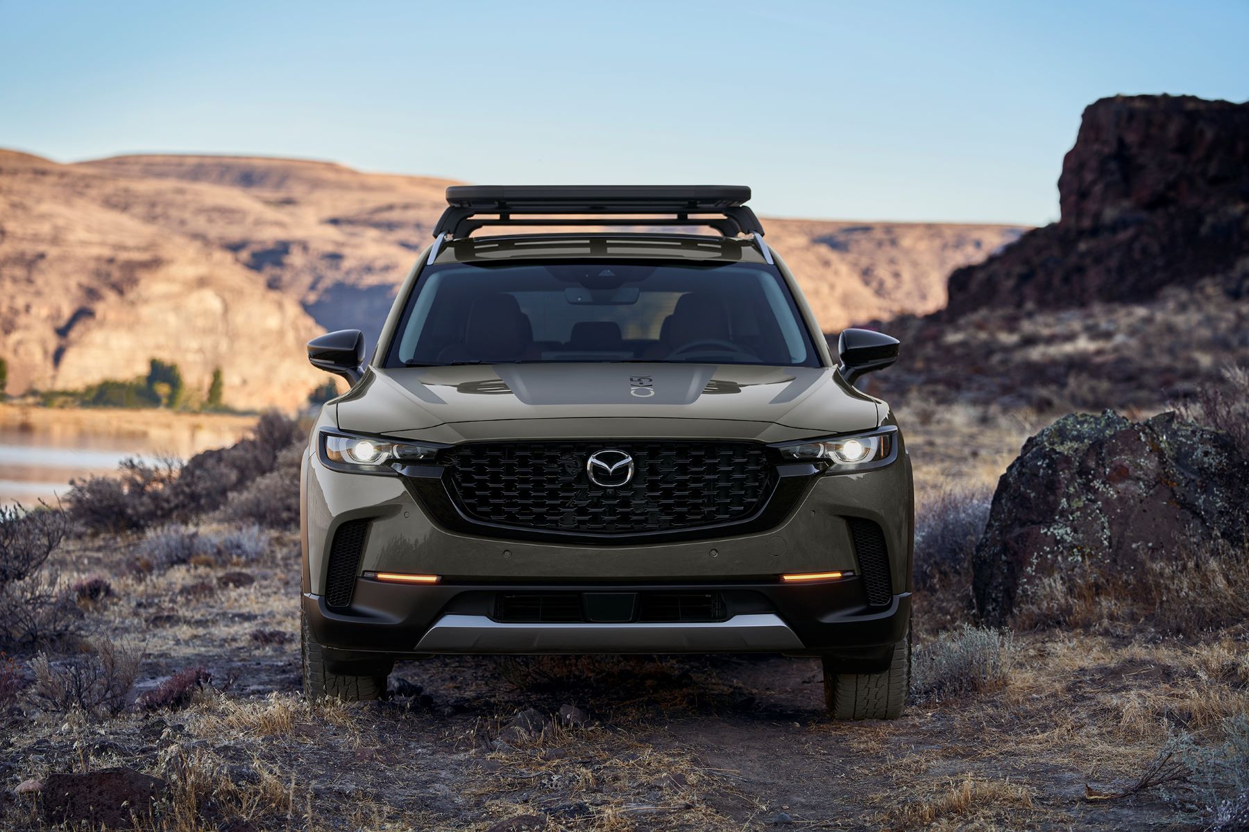 A 2023 Mazda CX-50 compact crossover SUV with a roof rack parked on off-road terrain