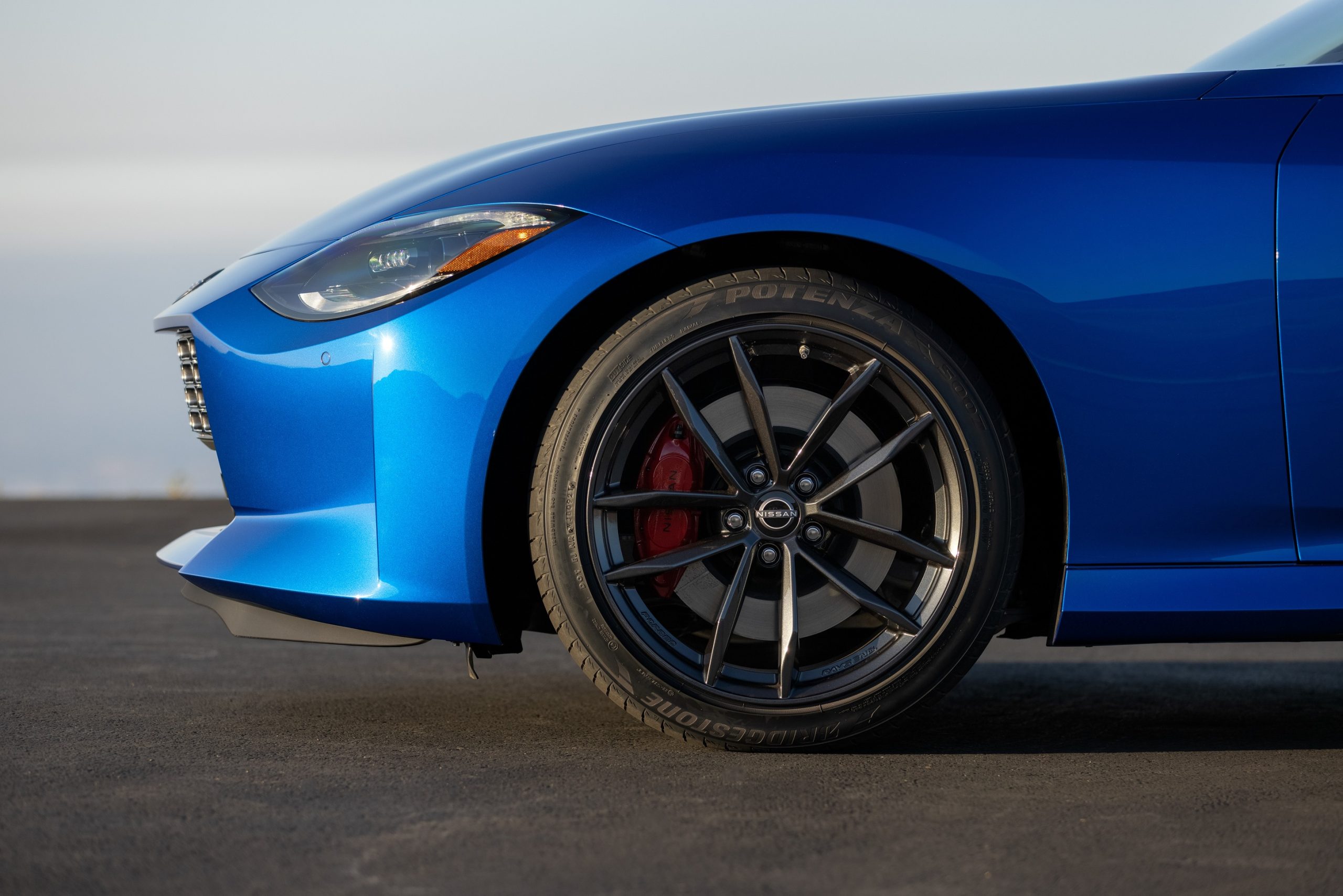 A side view of a blue 2023 Nissan Z Performance's front Bridgestone Potenza tire and black wheel