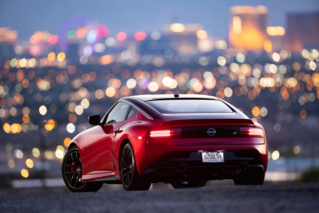 The rear 3/4 view of a red 2023 Nissan Z in front of the Las Vegas city lights