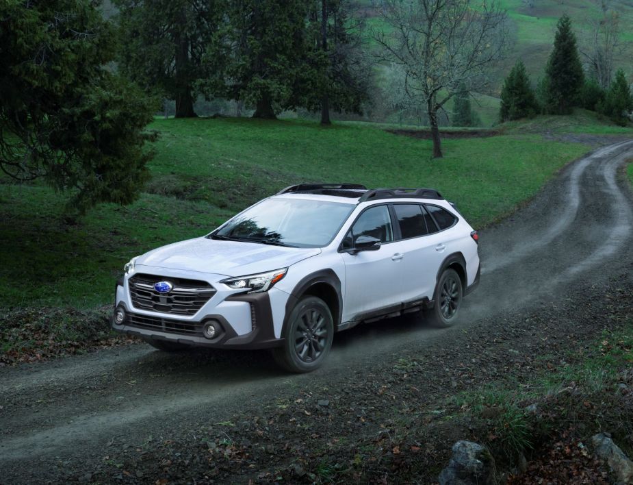The 2023 Subaru Outback midsize crossover SUV in white driving on a dirt forest trail at night