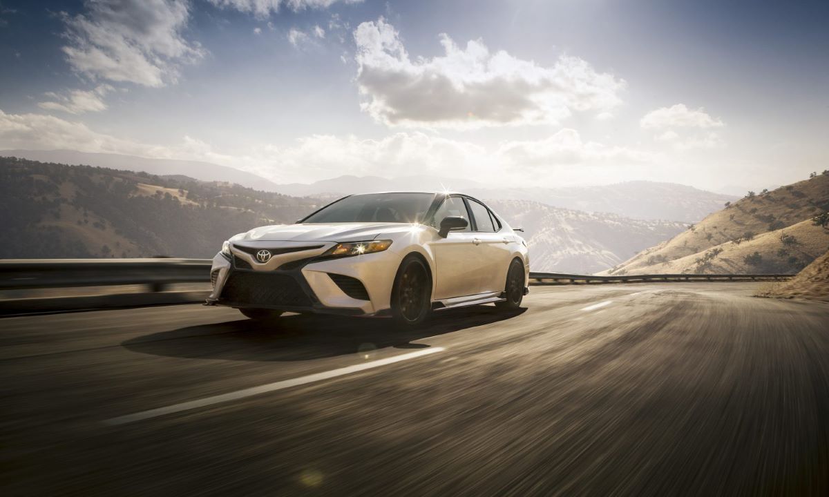 White 2023 Toyota Camry midsize sedan driving at high speeds along a mountain highway
