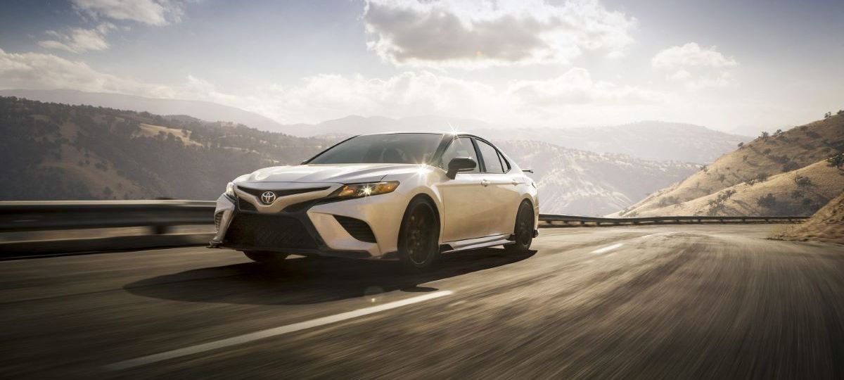 White Toyota TRD driving along a mountain road; the 2023 Camry midsize sedan will include a TRD variant