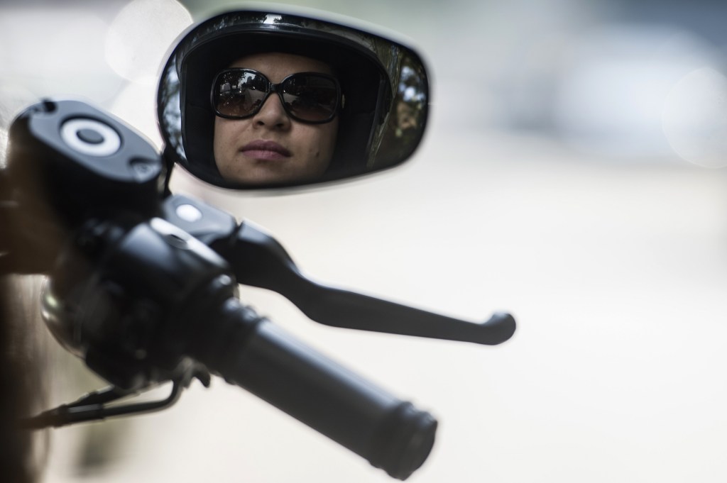 A female motorcycle rider wearing a helmet and sunglasses reflected in her mirror
