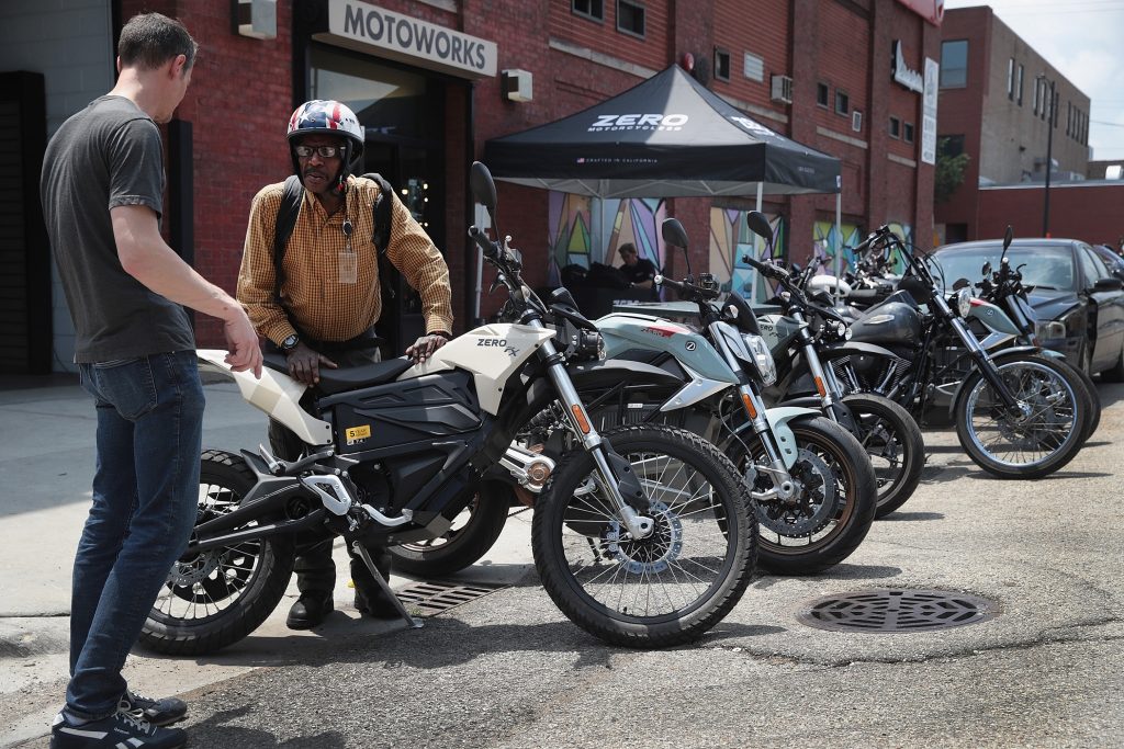 A rider dressed in yellow and a MotoWorks Chicago employee in a black shirt near a line of street-legal 2019 Zero electric motorcycles