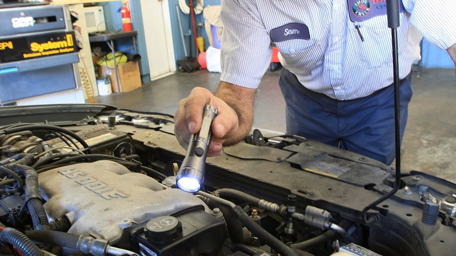 A technician visually inspects a car engine bay with a flashlight as part of an emissions test in California