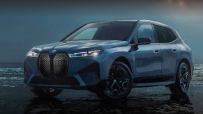 A blue 2022 BMW iX electric luxury SUV is parked with water in the background.