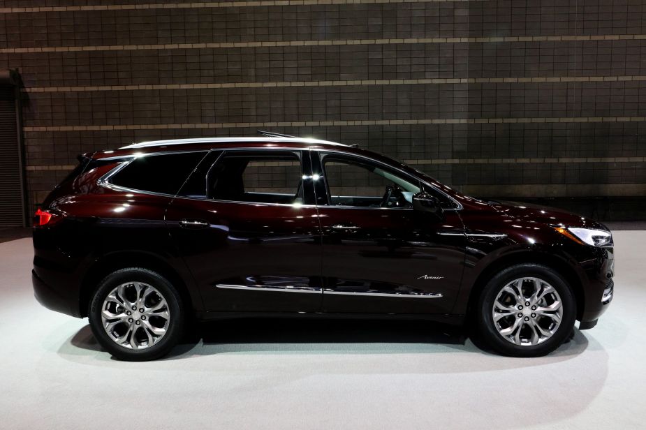 A dark maroon colored Buick Enclave, a luxury SUV, with a dark background and a light colored floor. 