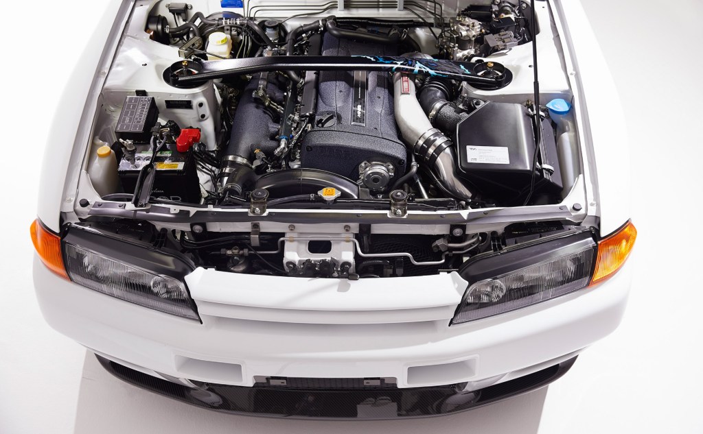 The black-covered 2.8-liter Mine's-built RB26 engine and titanium strut-tower brace in the engine bay of a white Built by Legends Mine's R32 Nissan Skyline GT-R