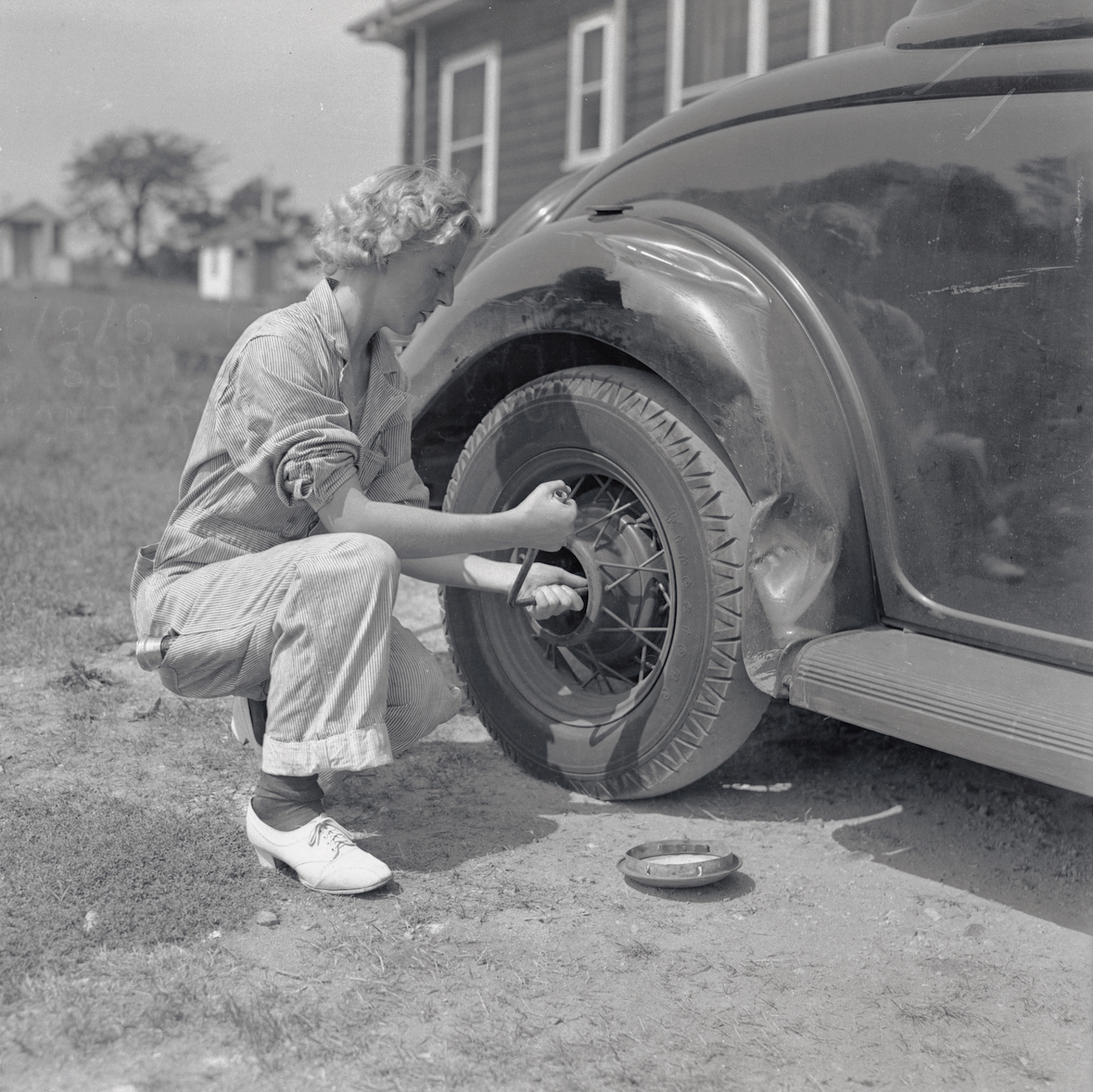 Black and white photo of a pioneering young female mechanic changing a tire in 1937.