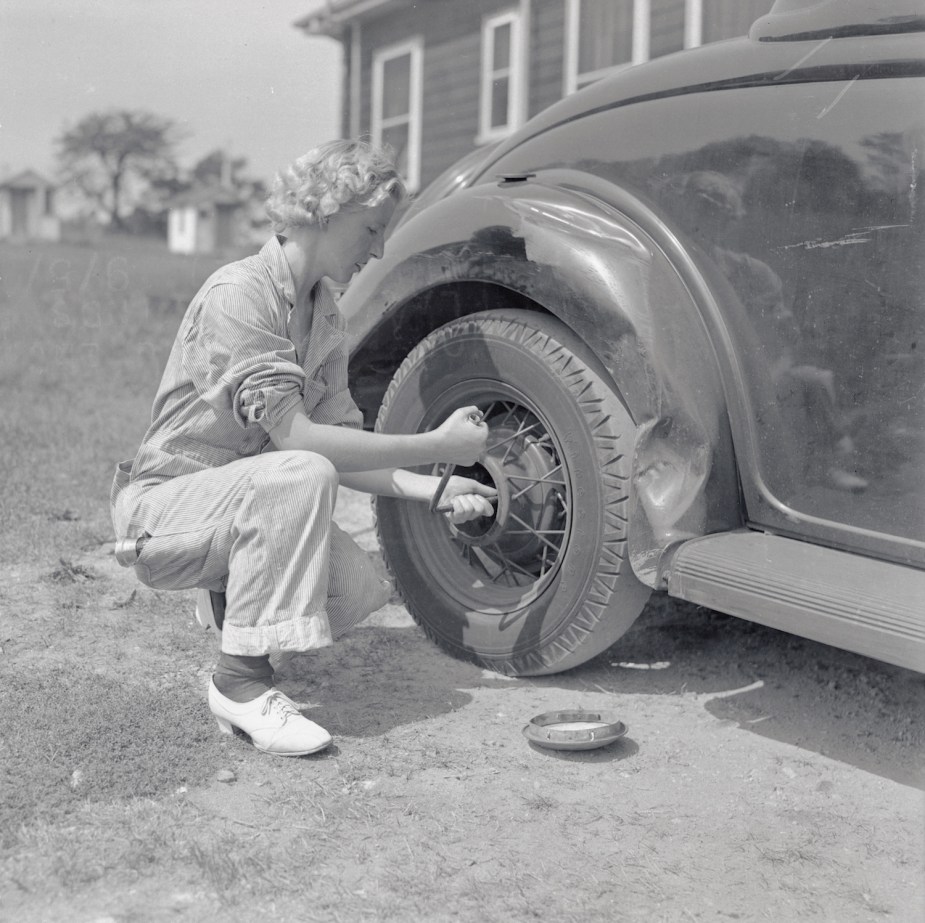 Black and white photo of a pioneering young female mechanic changing a tire in 1937.