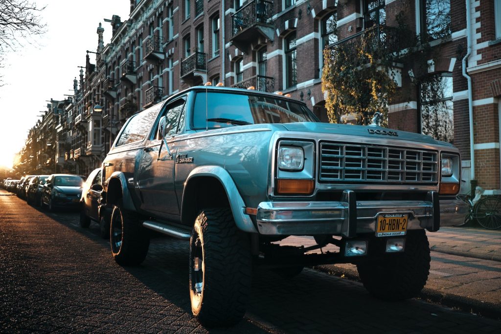 Blue Dodge Ram Charger with a lift kit parked on a city street, the sun setting behind it.