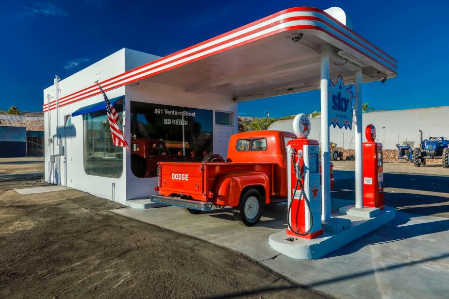 a vintage red pickup truck parked at an old timey gas station