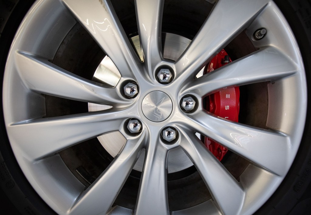 A close-up view of a Tesla Model X's disc brake and wheel during electric car maintenance