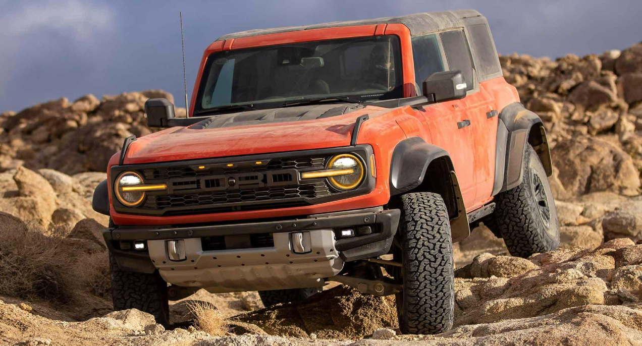 A red 2022 Ford Bronco Raptor off-road SUV is driving over rocks. 