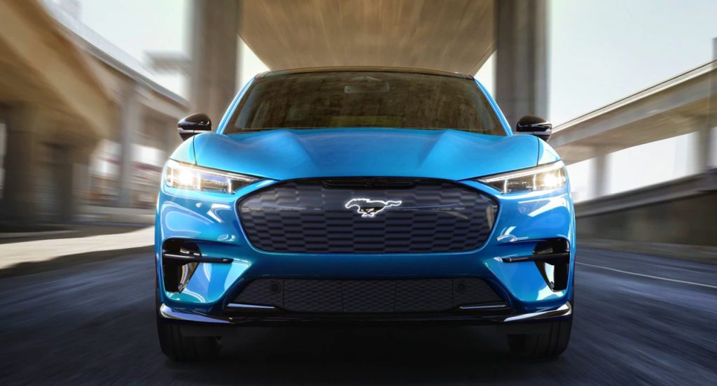 A blue 2022 Ford Mustang Mach-E electric SUV is driving on the road. 