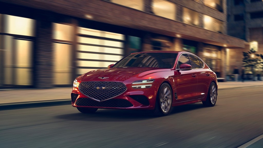 a red 2022 genesis g70 drives down a city street showing off its sports sedan prowess