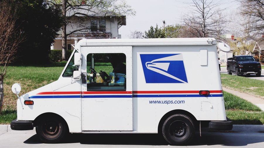 A Grumman LLV mail truck sits in a local neighborhood with USPS livery.