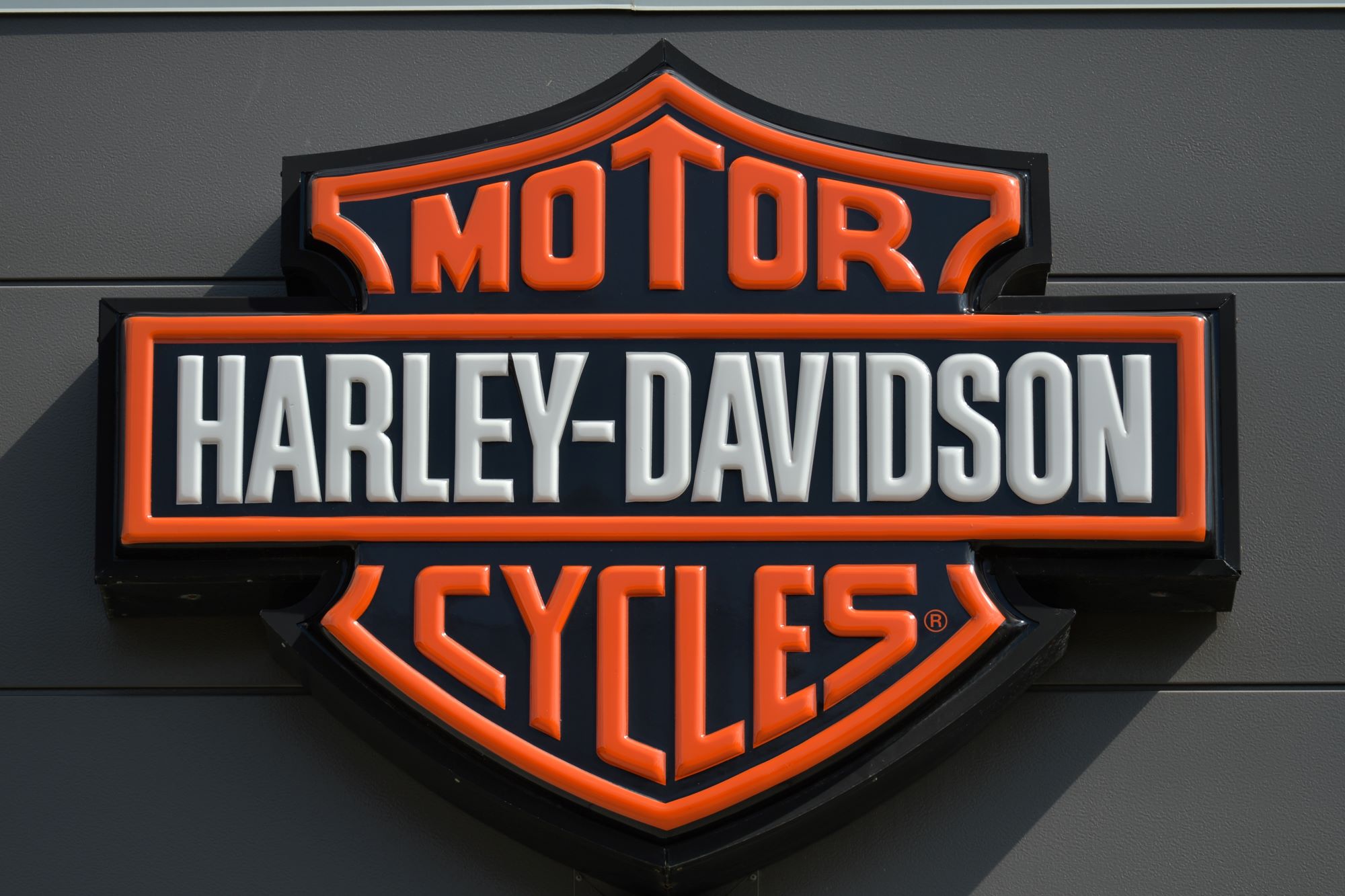 A black, orange, and white Harley-Davidson logo, creator of the 2022 Harley-Davidson Nightster.