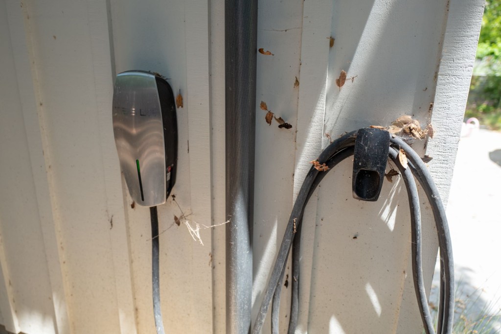 A Tesla home EV charger hanging on a wall in a garage area.