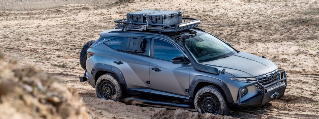 Gray Hyundai SUV with a roof rack and a winch parked in the desert, its 4x4 tires buried in the sand.