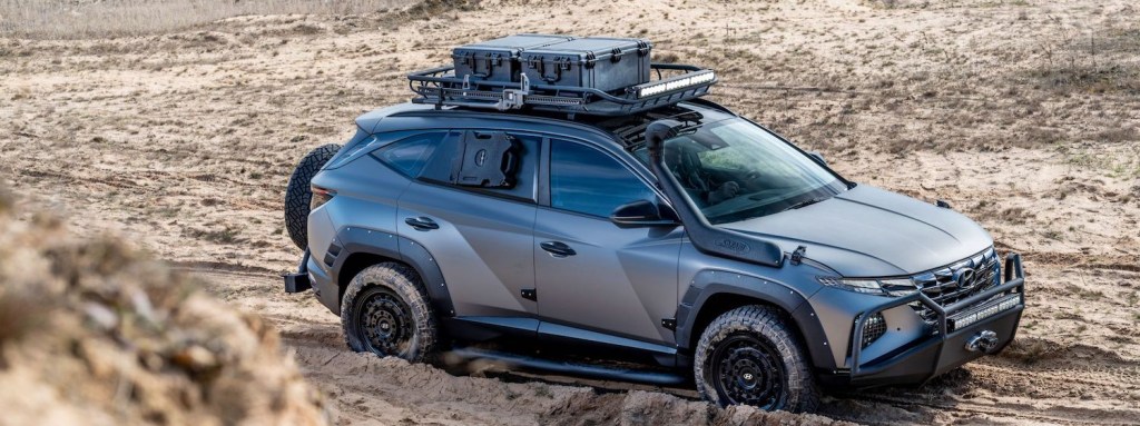 Gray Hyundai SUV with a roof rack and winch parked in the desert, its 4x4 tires buried in sand.