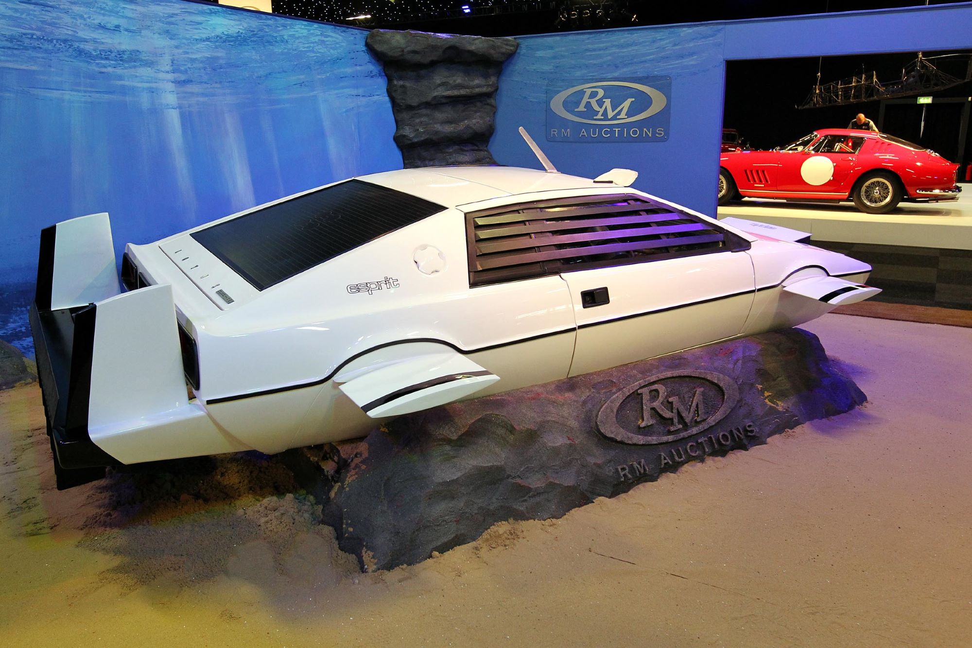 The white James Bond submarine car, used as inspiration for the Tesla Cybertruck, in front of a blue display indoors.