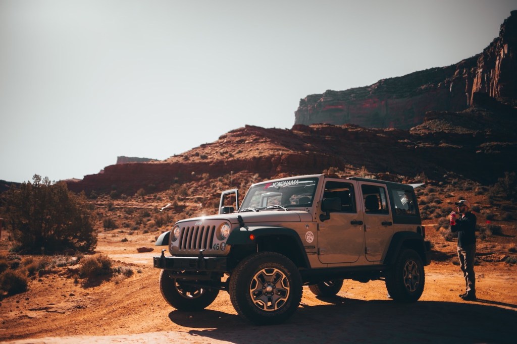 Gray Jeep Wrangler parked in the desert while someone opens its tailgate.
