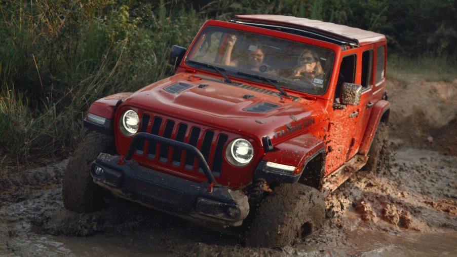 Red Jeep Wrangler driving through mud while off road.