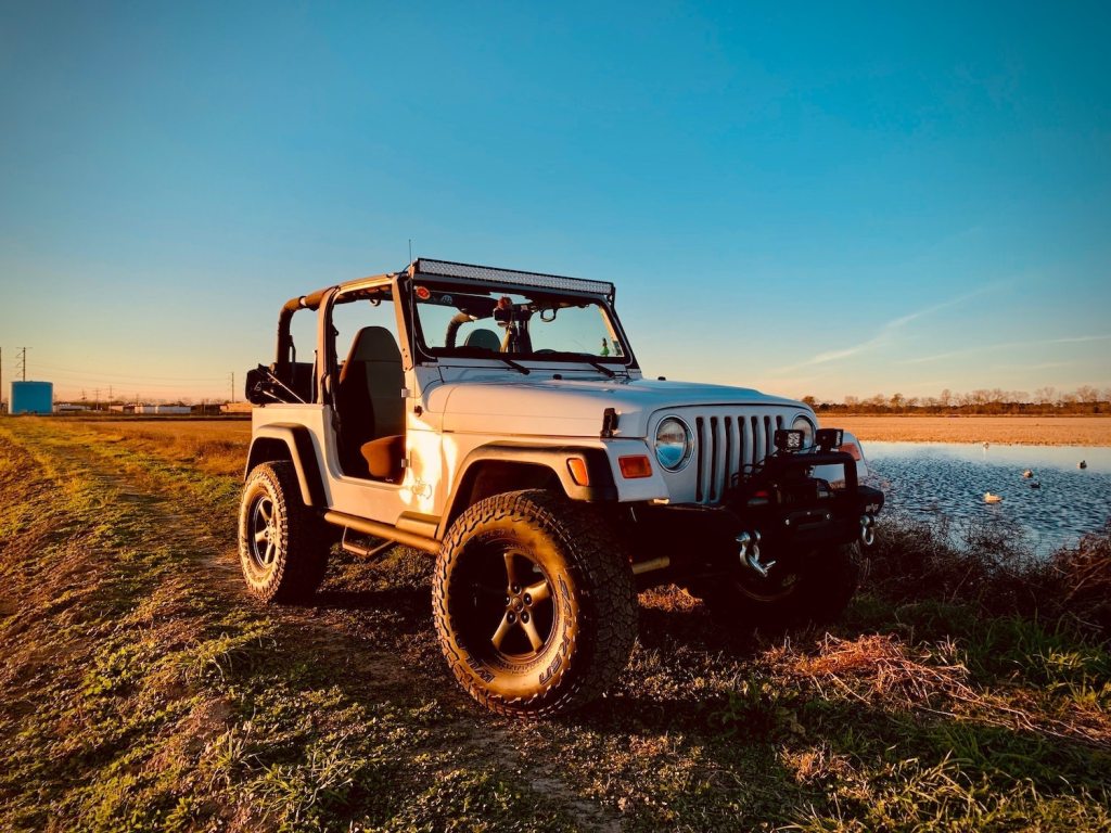 The white Jeep Wrangler two-door convertible SUV parked in a field by a pond.
