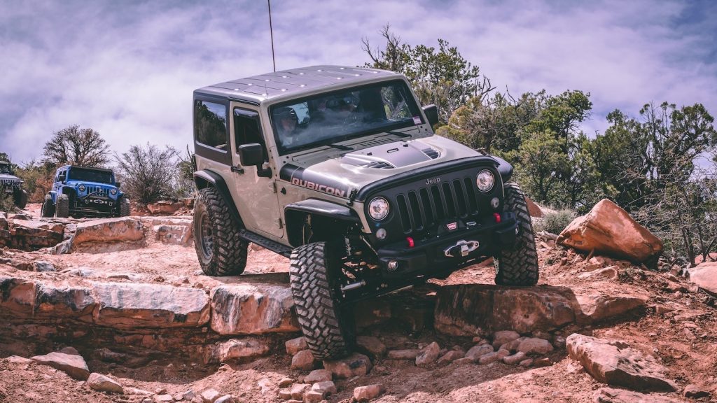 Gray Jeep Wrangler Rubicon navigating a rock in a 4x4 offroad trail. 