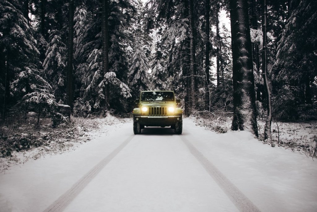 Jeep Wrangler SUV parked on a snowy road, lined with evergreen trees.