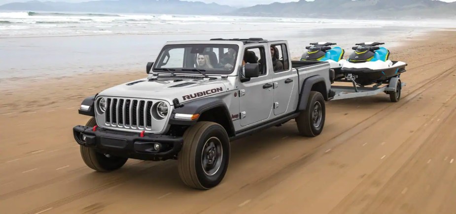 The 2022 Jeep Gladiator shows off its capability as a mid-size truck, it tows two watercraft on a beach.
