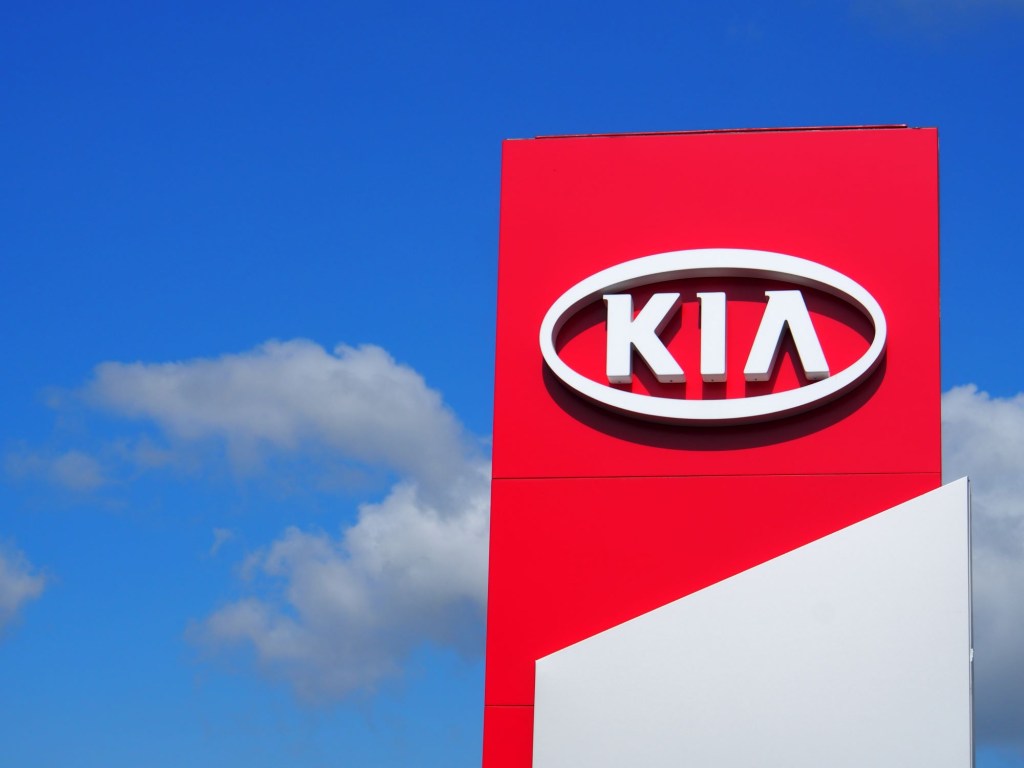 A white and red Kia sign in front of a blue and slightly cloudy sky. 